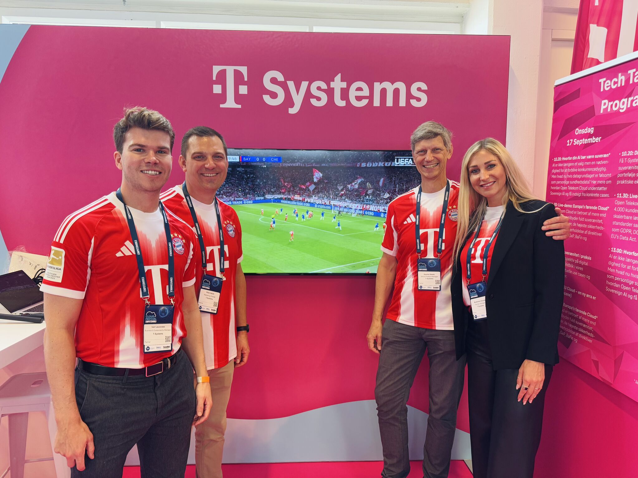 Vier Personen in FC Bayern München Trikots am T-Systems Stand, im Hintergrund läuft ein Fußballspiel auf einem Bildschirm