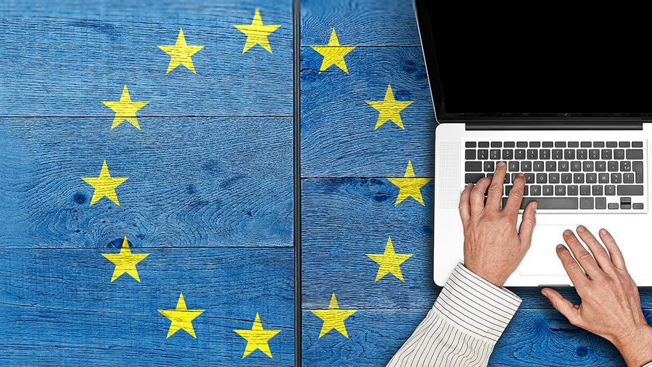 Person typing on a laptop keyboard on a blue wooden table, surrounded by yellow stars from the EU flag.